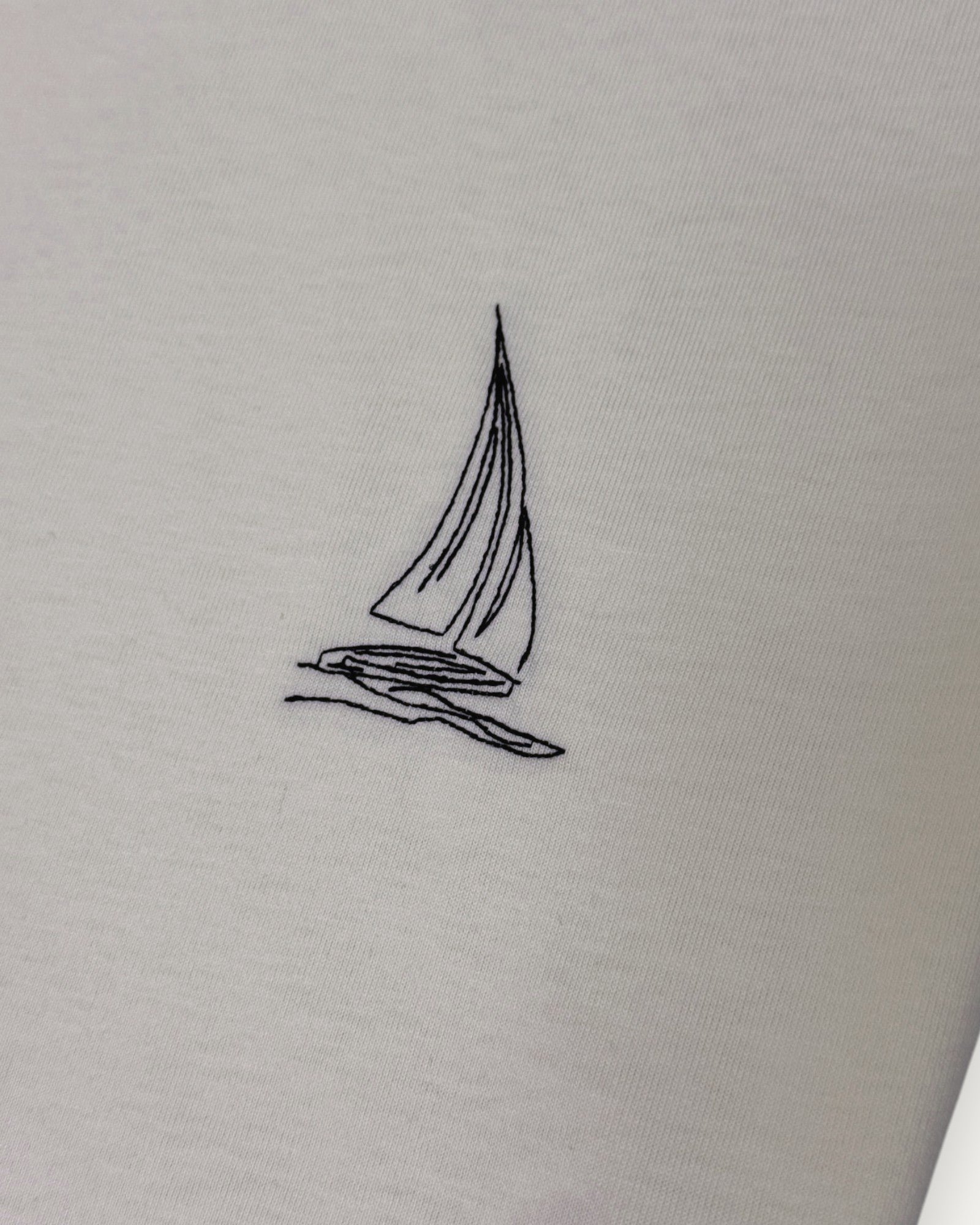 Embroidered sailboat design on an off white cream fabric background